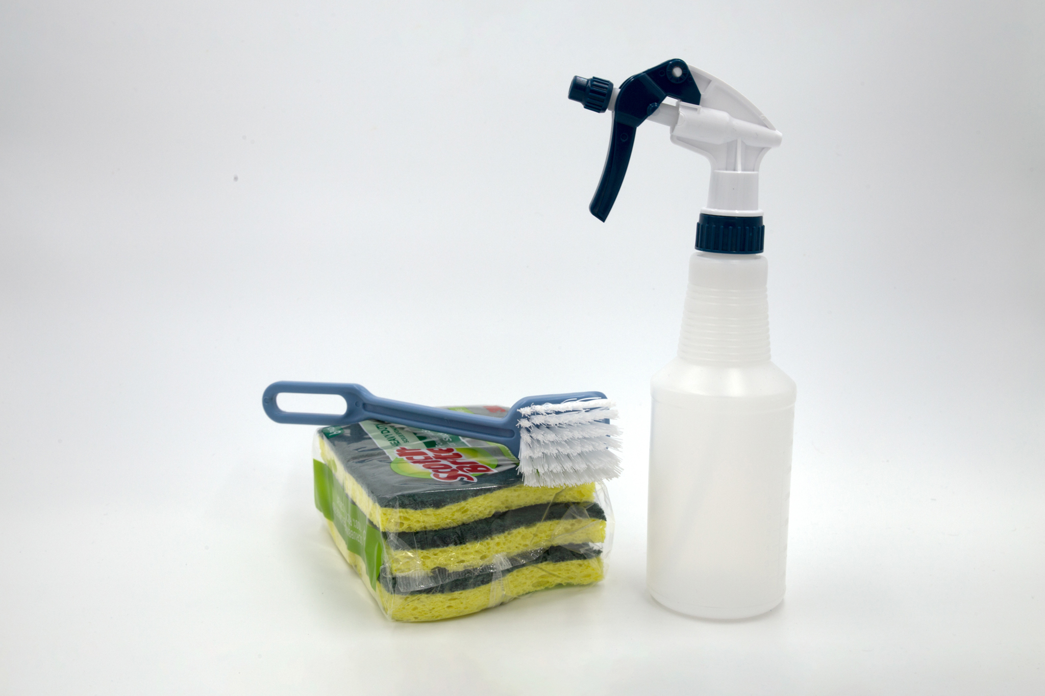 A sponge, spray bottle, and cleaning brush on a white background